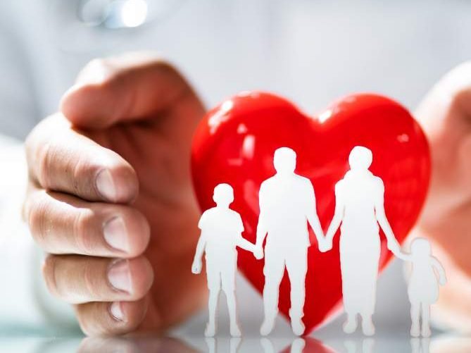 Hands protecting a red heart and a paper family
